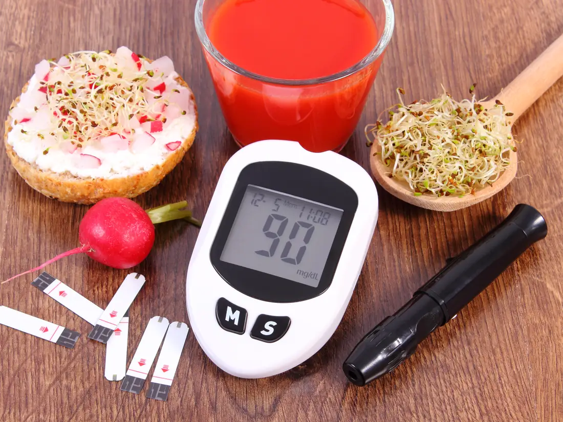 Blood glucose meter beside a whole-grain open sandwich, sprouts, radish and tomato juice