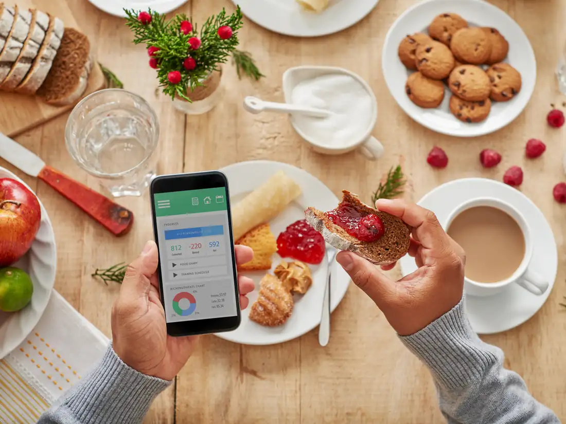 Person tracking a meal on a smartphone app while eating breakfast, like keeping a food and symptom journal