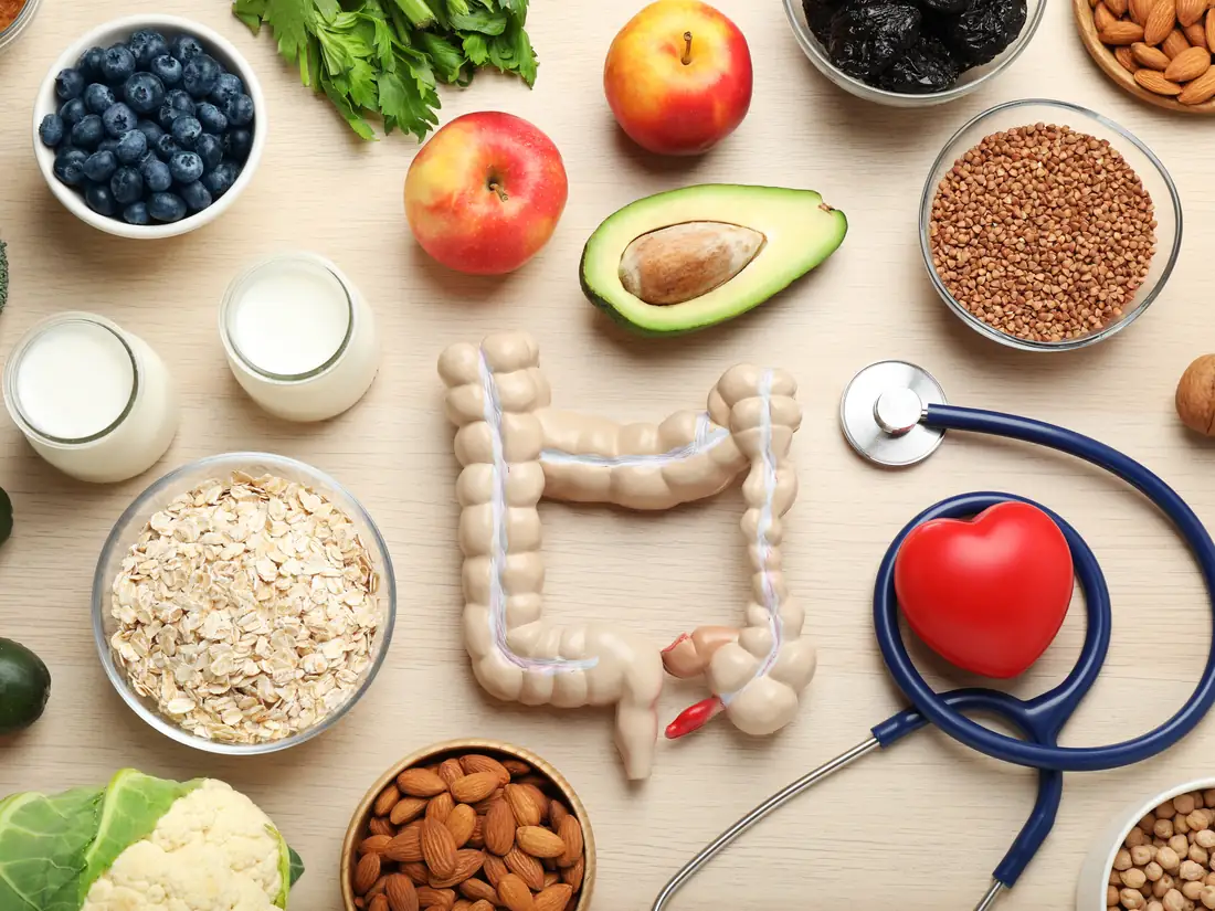 Gut-friendly whole foods including oats, yogurt, blueberries, broccoli, avocado and almonds around a model of the digestive tract