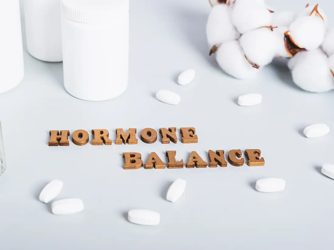 The words hormone balance spelled in wooden letters beside supplement bottles and cotton flowers