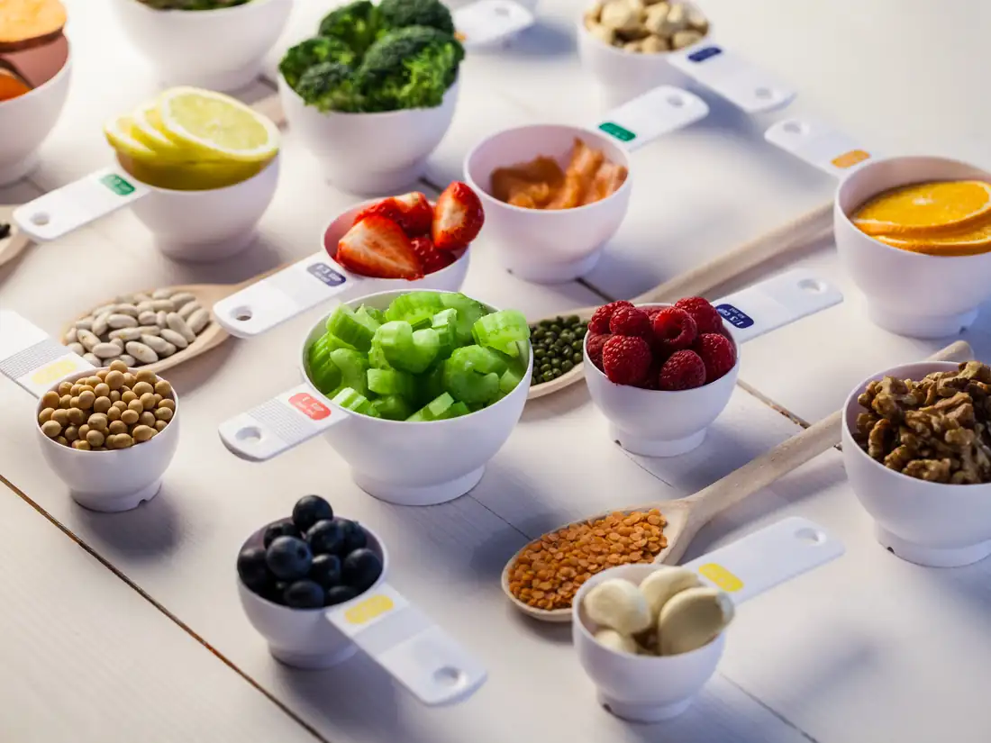 Measuring cups filled with broccoli, berries, beans, lentils, walnuts, citrus and other nutrient-rich whole foods