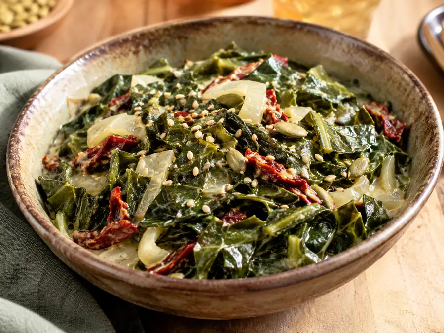 Creamy collard greens with sun-dried tomatoes, onion and seeds in a stoneware bowl
